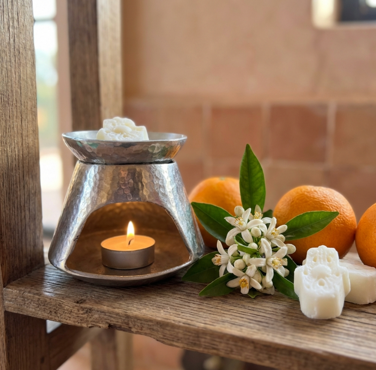 Galet de fondant parfumé Mïnek en train de fondre dans un brûle-parfum, avec bougie chauffe-plat et fleurs d'oranger
